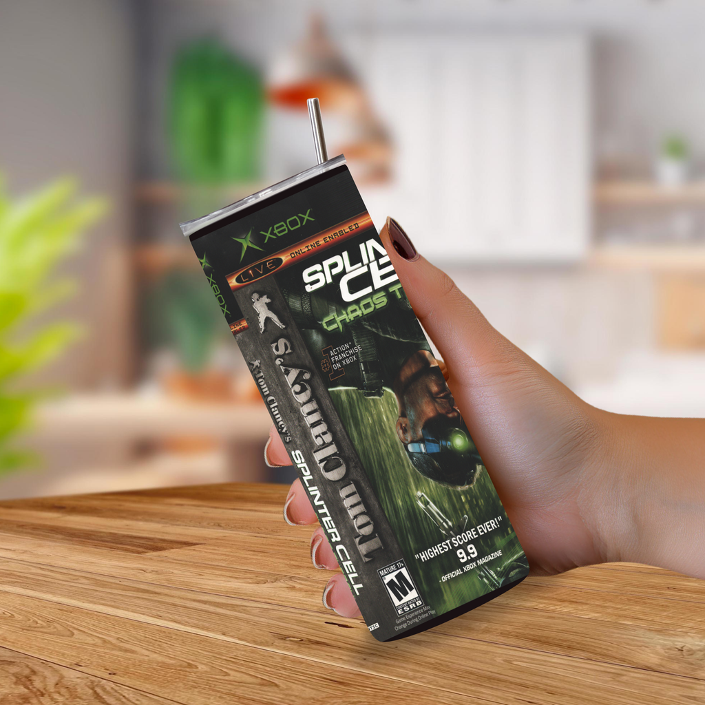A hand holding a custom 20oz tumbler styled like an Xbox game, featuring "Splinter Cell Chaos theory" on a wooden table with a blurred kitchen background.