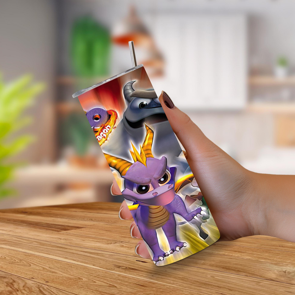 A hand holds a 20oz stainless steel tumbler with a printed wraparound design featuring the video game character Spyro Year of the Dragon with a metal straw, against a blurred indoor background.