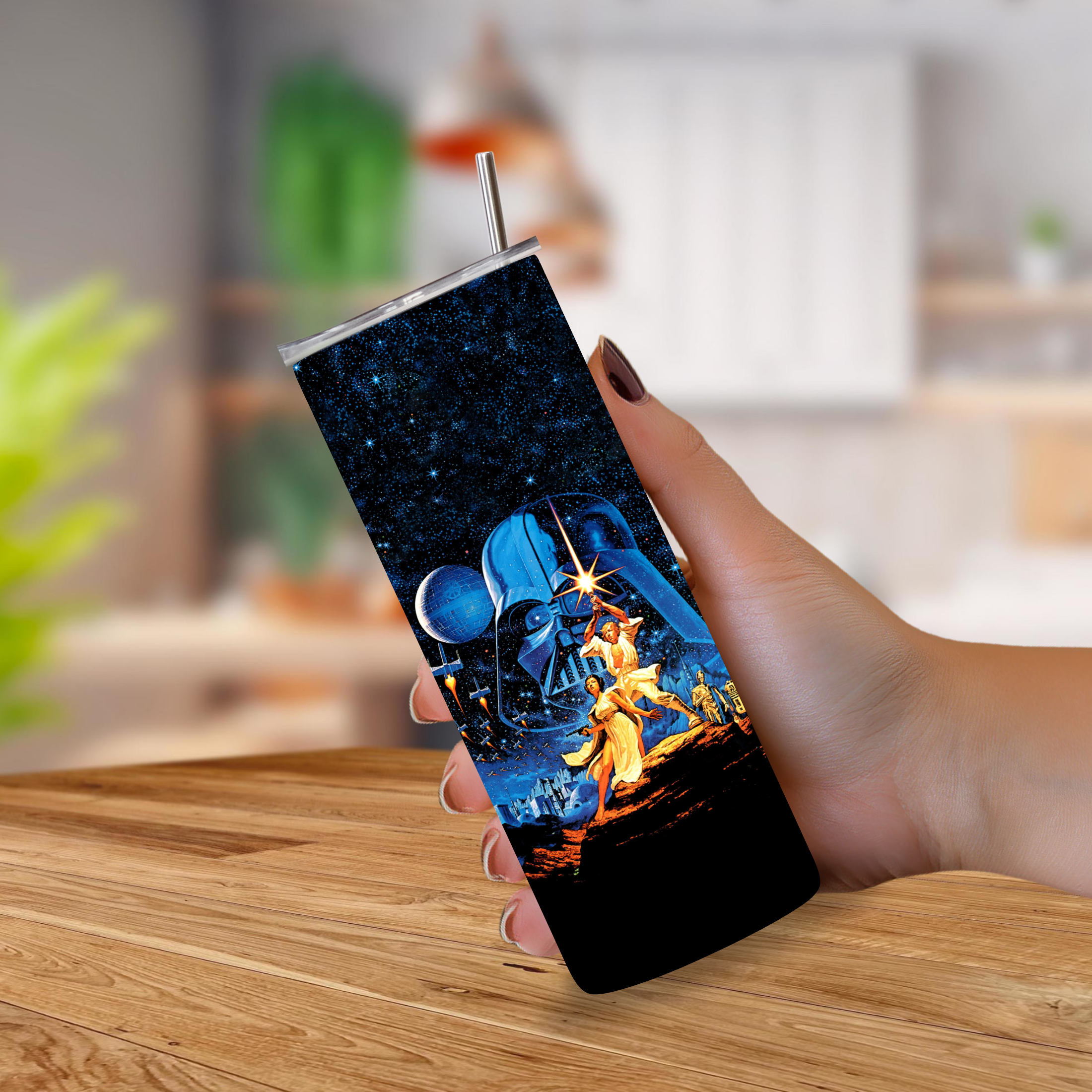 A hand holding a slim stainless-steel tumbler with a printed 1977 Star Wars graphic, set against a blurred kitchen background.