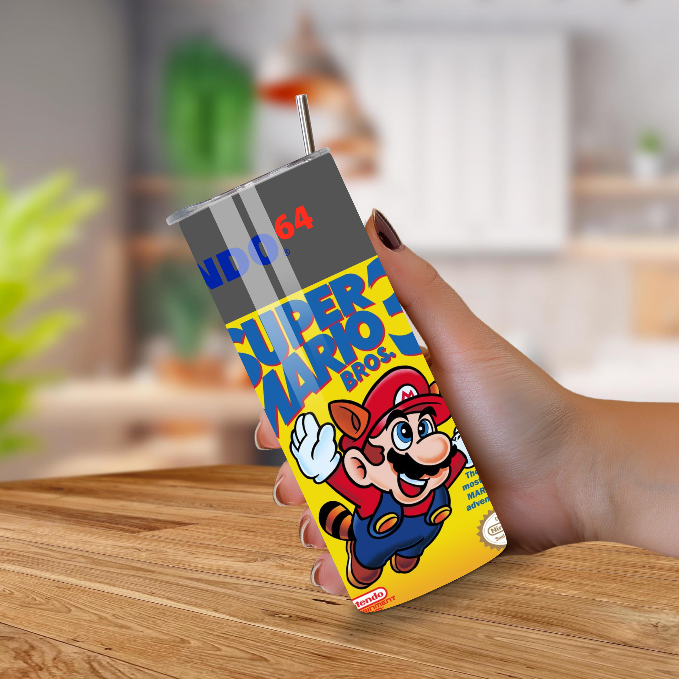 Hand holding a Super Mario Bros. themed tumbler on a wooden surface with a blurred background