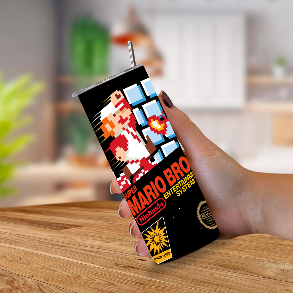 A hand holding a tall, slim 20oz tumbler drink can featuring NES Super Mario Bros. pixel art and Nintendo branding, set against a blurred kitchen background with a wooden table in the foreground.