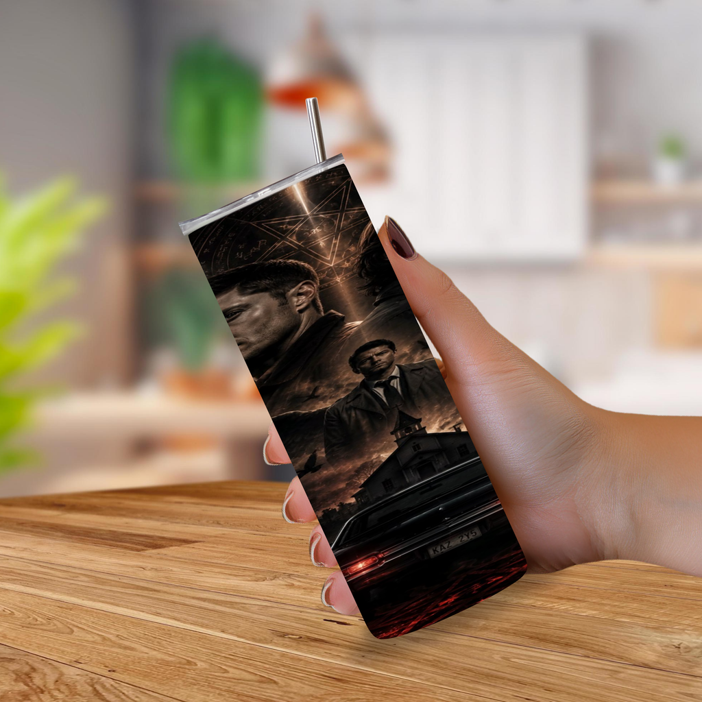 A hand holding a tall, insulated tumbler with a metal straw, featuring a dark cinematic print the TV show Supernatural, set against a blurred kitchen background.