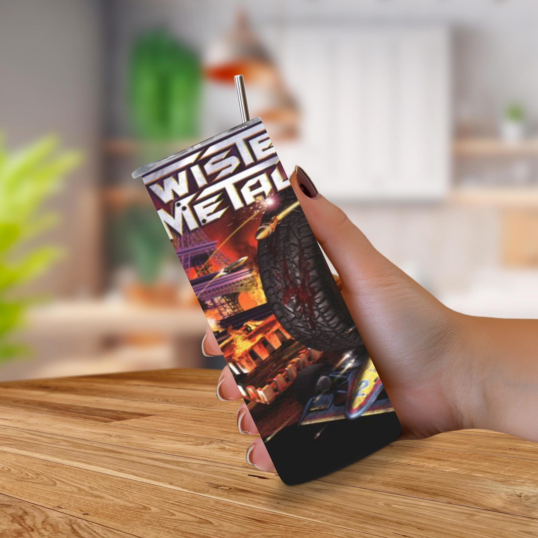 A hand holding a slim 20oz tumbler with a printed TWISTED METAL 2 logo and colorful sci-fi artwork, featuring a clear straw, against a blurred indoor background with a wooden table.