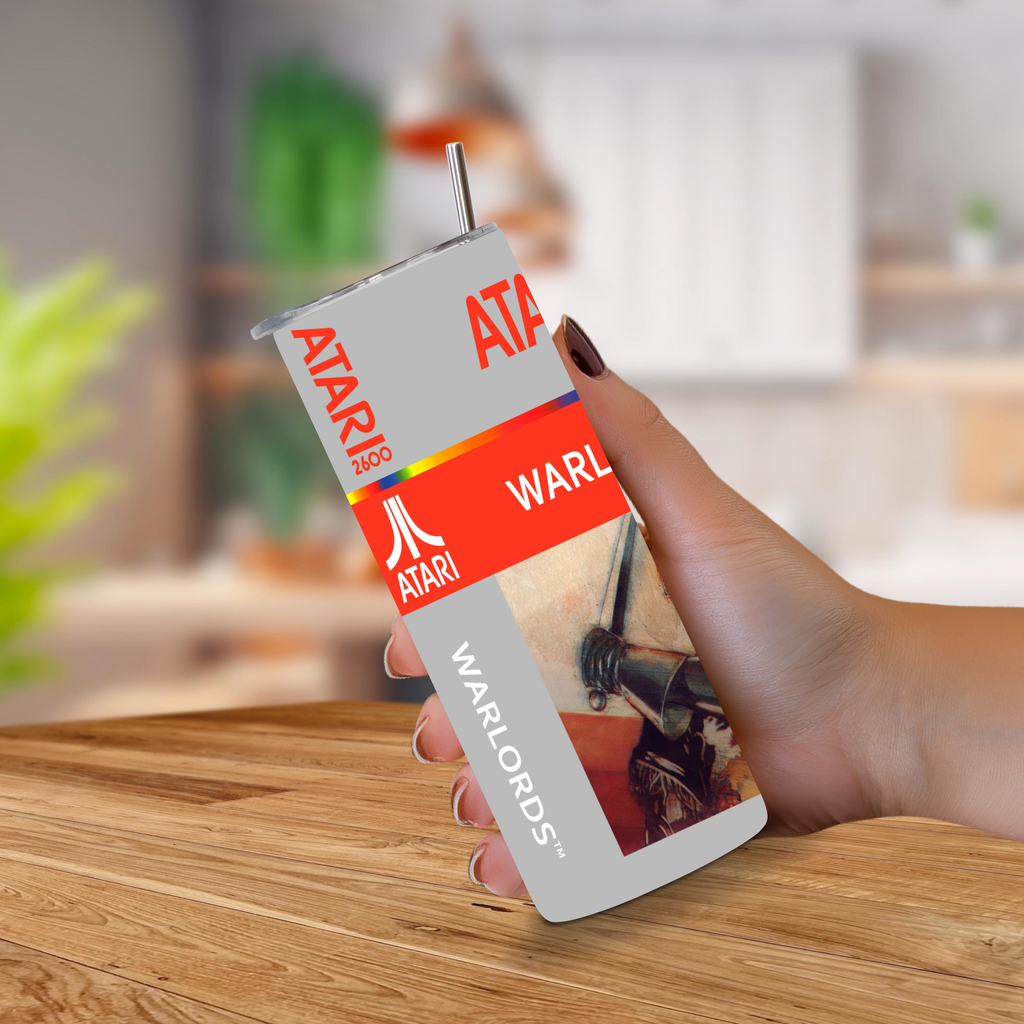 A hand holding a retro Atari Warlords 20oz stainless steel tumbler with a straw, set against a blurred kitchen background.