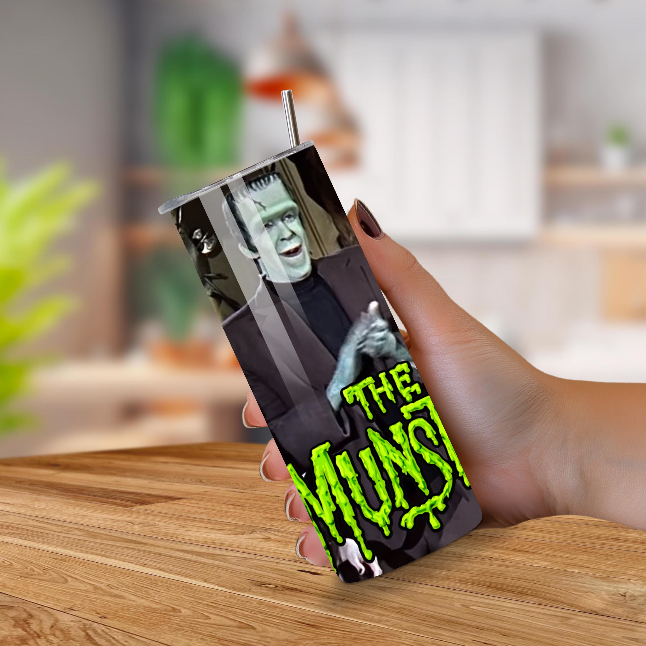 Person holding a tumbler with 'The Munsters' design on a wooden surface.